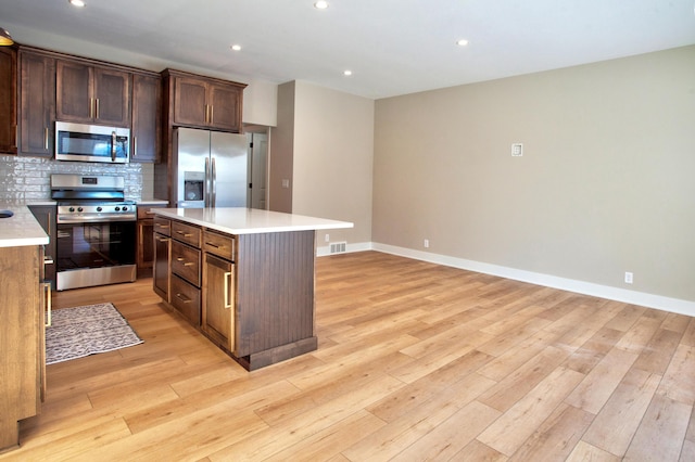 kitchen featuring visible vents, a kitchen island, light wood-type flooring, decorative backsplash, and stainless steel appliances