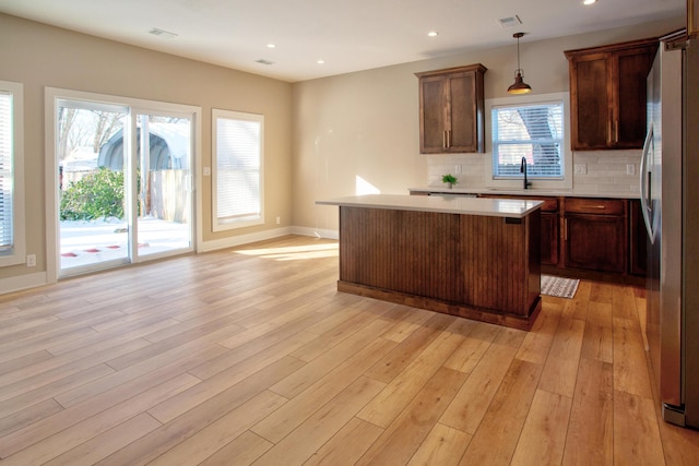 kitchen with tasteful backsplash, a center island, light countertops, light wood-style flooring, and freestanding refrigerator