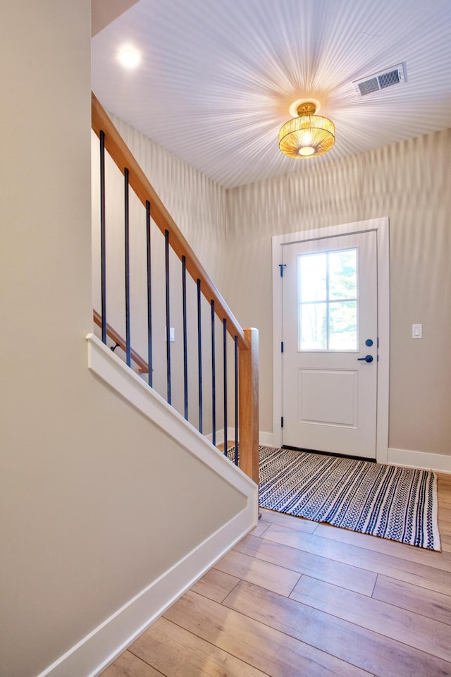 foyer entrance with visible vents, baseboards, wood finished floors, and stairs