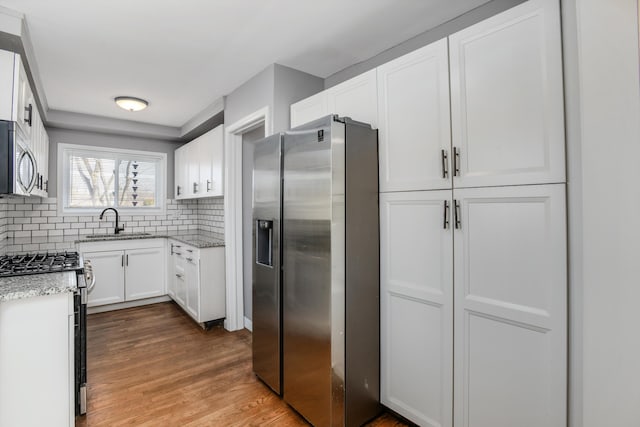 kitchen with wood finished floors, a sink, appliances with stainless steel finishes, white cabinetry, and backsplash