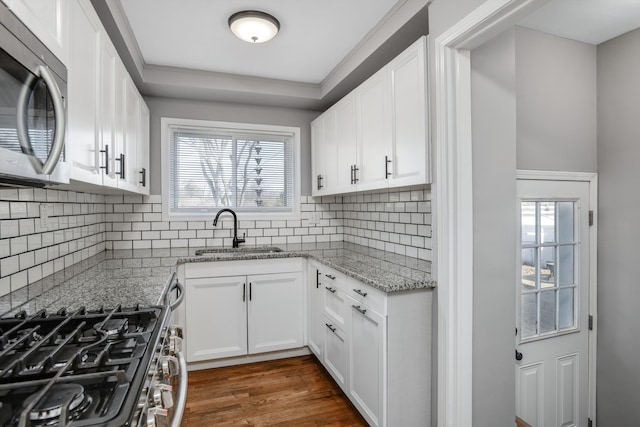 kitchen with light stone counters, dark wood-style flooring, a sink, appliances with stainless steel finishes, and white cabinetry