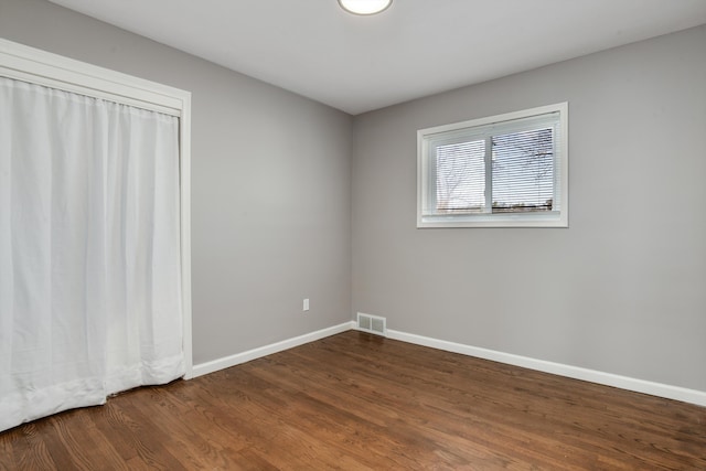 unfurnished room with dark wood-type flooring, visible vents, and baseboards