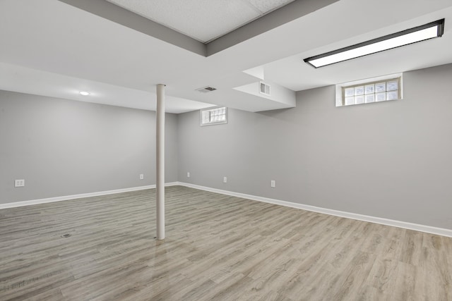 below grade area with baseboards, visible vents, and light wood finished floors