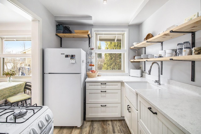 kitchen with wood finished floors, open shelves, freestanding refrigerator, a sink, and gas range oven