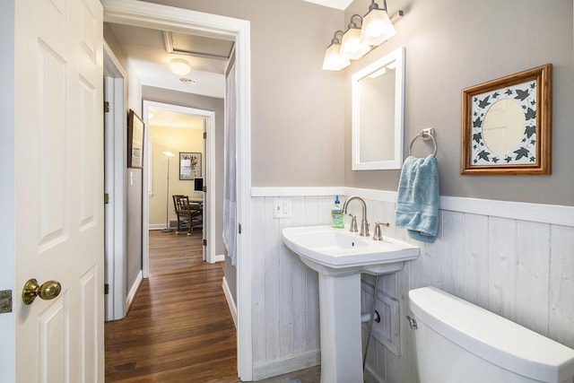 half bath with a sink, toilet, wood finished floors, and wainscoting