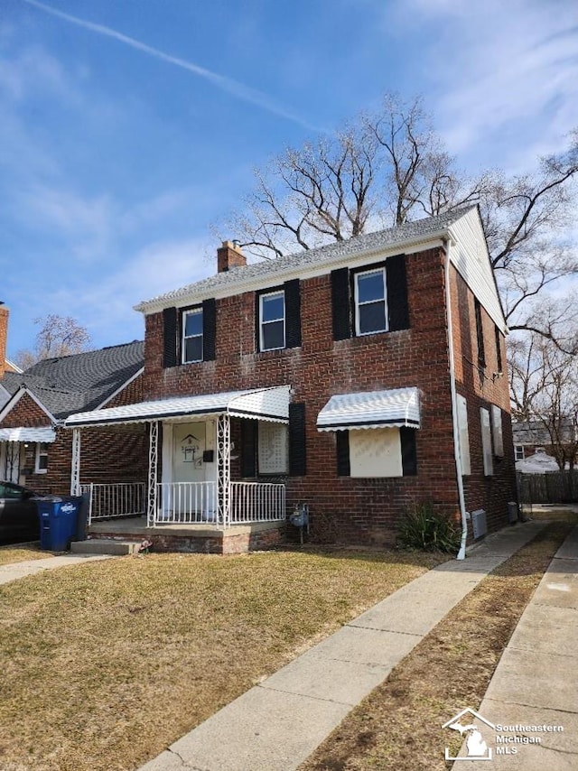 view of front of home featuring brick siding, covered porch, a chimney, and a front lawn