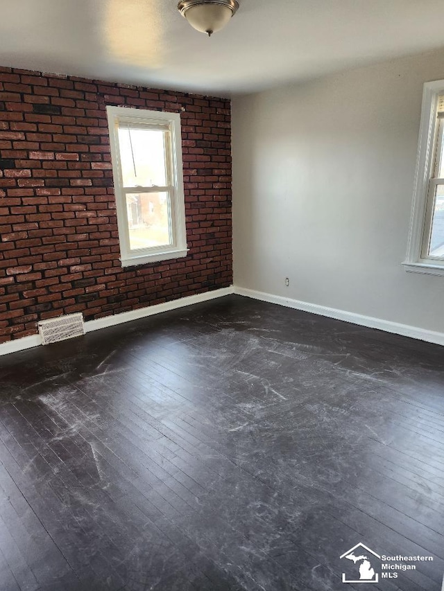 empty room with visible vents, baseboards, dark wood-style floors, and brick wall