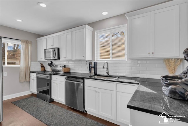 kitchen with dark countertops, decorative backsplash, white cabinets, stainless steel appliances, and a sink