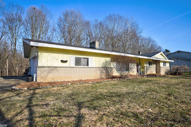 view of front of property featuring board and batten siding, a front lawn, brick siding, and a chimney