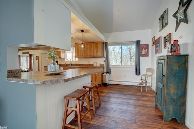 kitchen with a breakfast bar, baseboard heating, dark wood-style flooring, a peninsula, and a sink