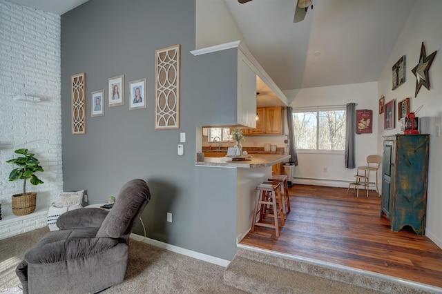 kitchen featuring baseboards, high vaulted ceiling, a sink, light countertops, and a kitchen bar