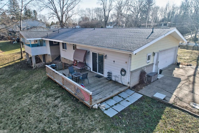 back of property with a deck, a detached garage, a yard, a shingled roof, and brick siding