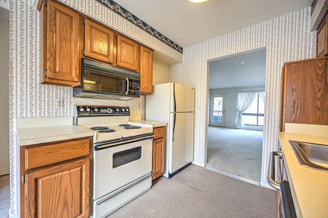 kitchen with white appliances, wallpapered walls, light countertops, light carpet, and brown cabinets