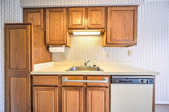 kitchen with a sink, wallpapered walls, brown cabinetry, light countertops, and dishwasher