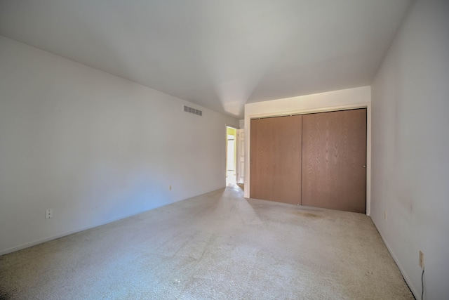 unfurnished bedroom featuring lofted ceiling, visible vents, a closet, and light carpet