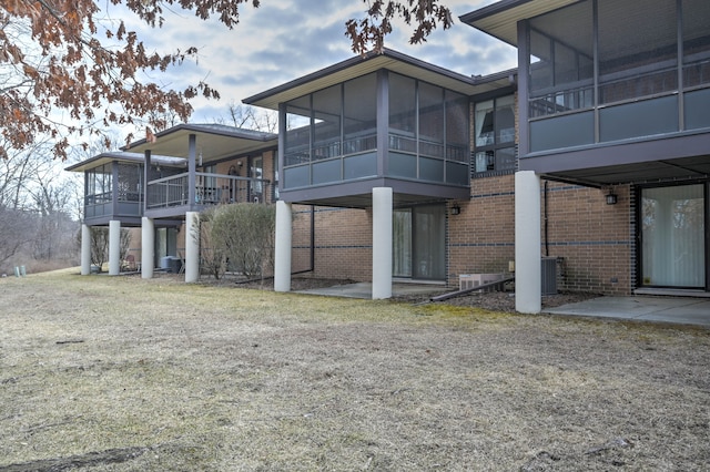 rear view of property featuring cooling unit, brick siding, and a sunroom