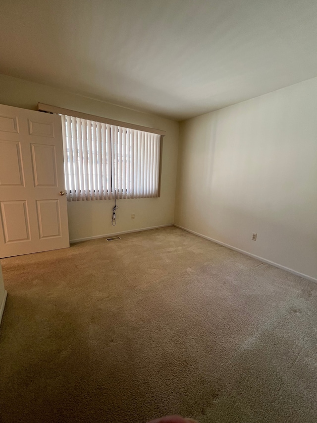 unfurnished room featuring visible vents, light colored carpet, and baseboards