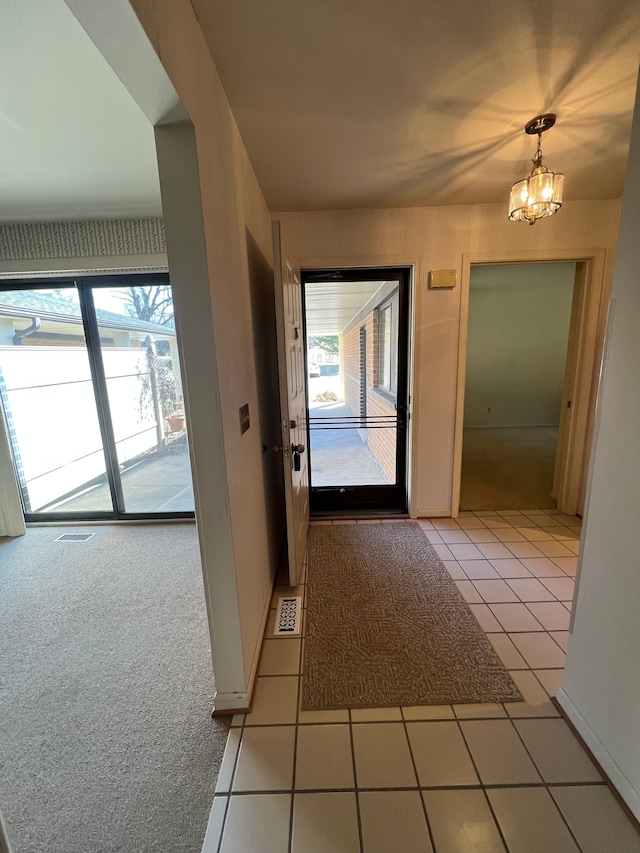 entrance foyer with a wealth of natural light, a notable chandelier, light colored carpet, and light tile patterned floors