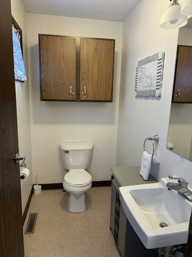 bathroom featuring visible vents, toilet, baseboards, and a sink