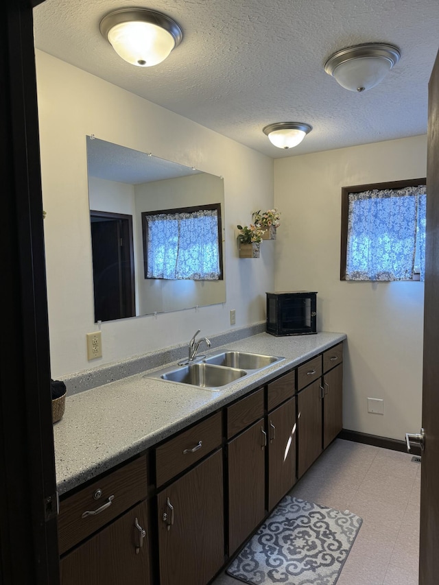 kitchen featuring baseboards, a sink, light countertops, dark brown cabinetry, and a textured ceiling