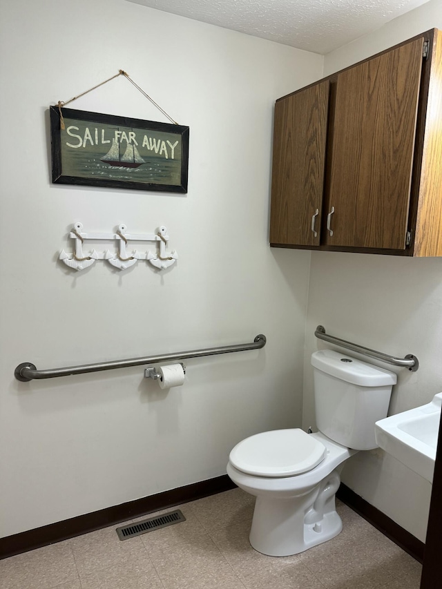 half bathroom featuring toilet, baseboards, visible vents, and a textured ceiling