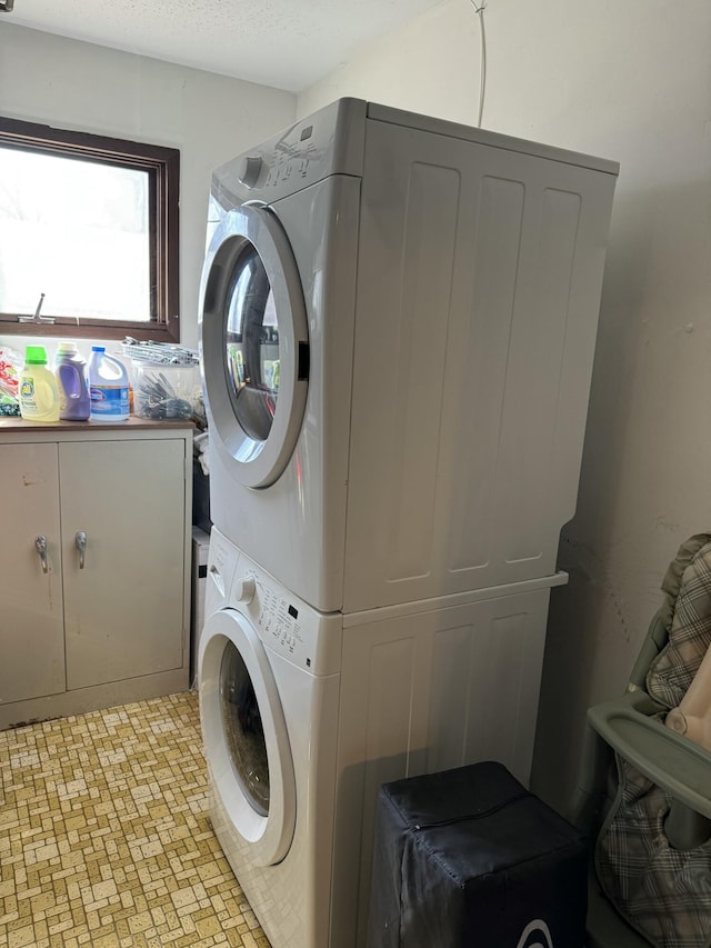 laundry room featuring cabinet space, stacked washer / drying machine, and a textured ceiling