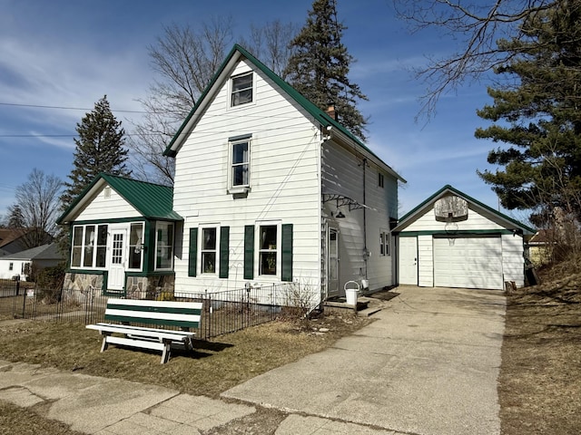 back of property featuring an outbuilding, driveway, a fenced front yard, a detached garage, and metal roof