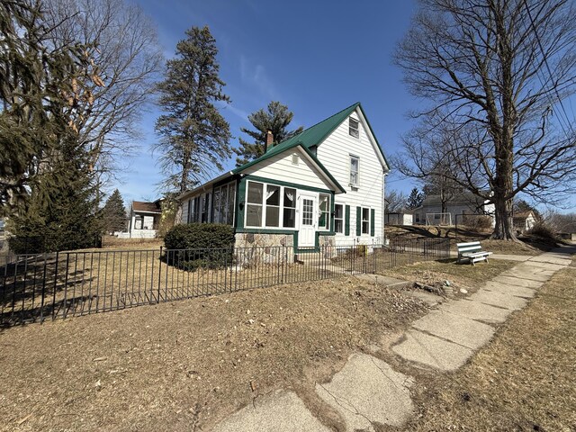 view of side of home featuring a fenced front yard, a chimney, and a sunroom