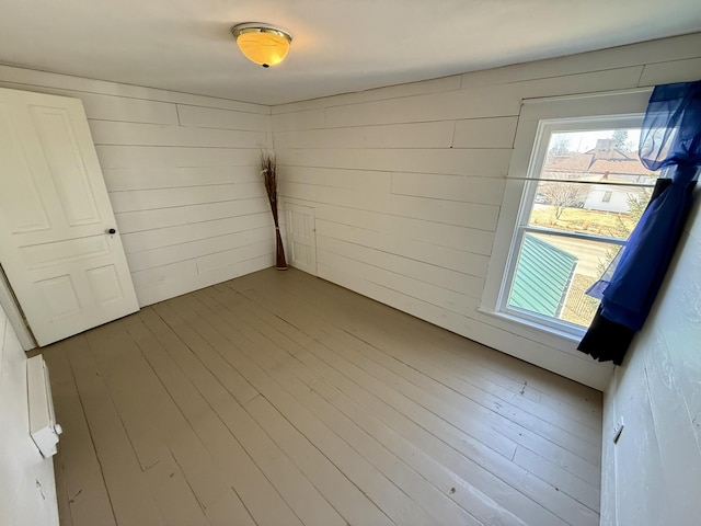 spare room featuring a healthy amount of sunlight, wood finished floors, and wood walls