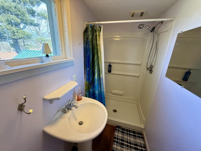 full bathroom featuring a textured ceiling, visible vents, a stall shower, and a sink