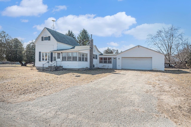 view of front of property with a garage, driveway, a chimney, and a sunroom