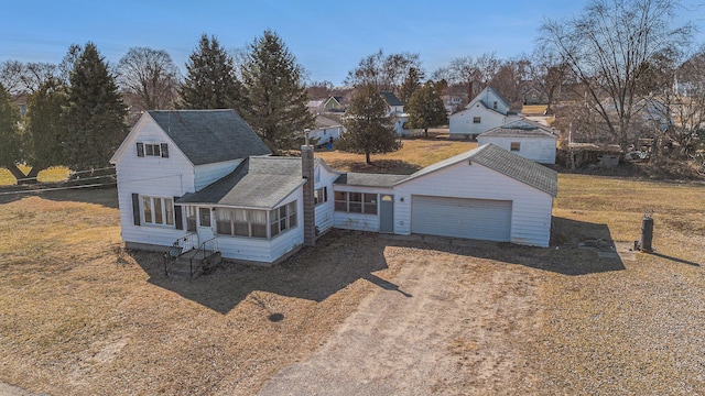 view of front facade with roof with shingles, a chimney, dirt driveway, and a sunroom