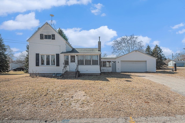 view of front of home featuring an attached garage, entry steps, a chimney, a sunroom, and driveway