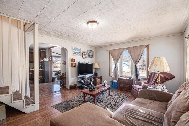 living room featuring visible vents, wood finished floors, arched walkways, baseboards, and stairs