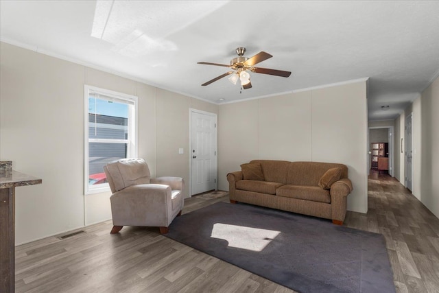 living area featuring ceiling fan, visible vents, wood finished floors, and ornamental molding