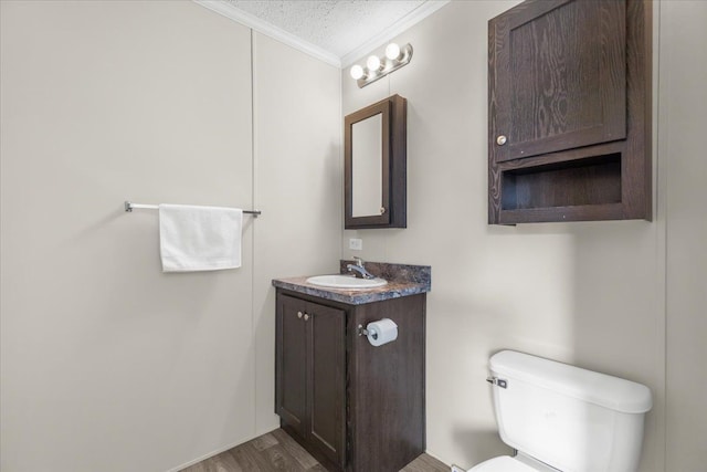 bathroom featuring toilet, vanity, ornamental molding, wood finished floors, and a textured ceiling