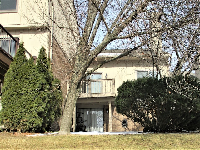 back of property with a yard, brick siding, and a balcony