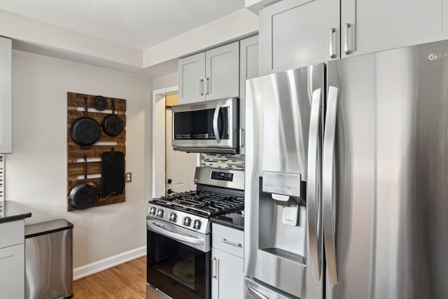 kitchen featuring baseboards, dark stone counters, decorative backsplash, light wood-style flooring, and appliances with stainless steel finishes