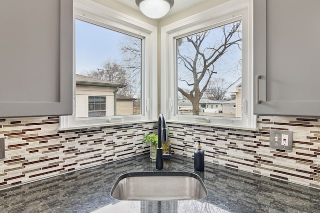 kitchen with a sink, tasteful backsplash, a healthy amount of sunlight, and dark stone countertops