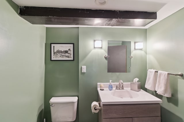 half bath with vanity, beamed ceiling, and toilet