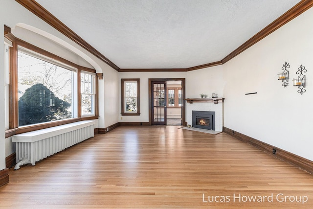 unfurnished living room with a wealth of natural light, a fireplace with flush hearth, light wood-style flooring, and radiator heating unit