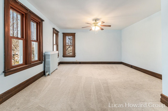 unfurnished room featuring light colored carpet, baseboards, radiator, and a ceiling fan