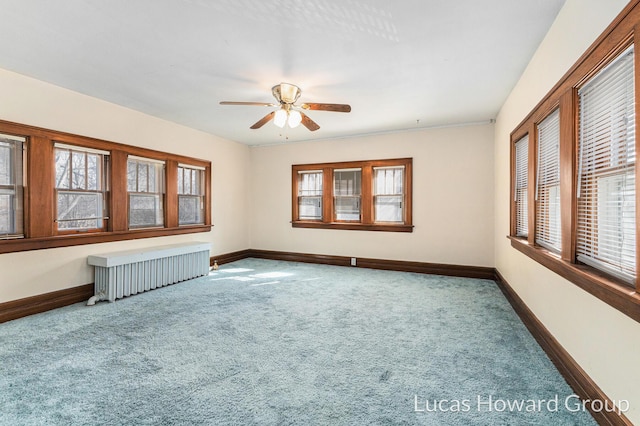 carpeted empty room featuring a wealth of natural light, ceiling fan, radiator, and baseboards