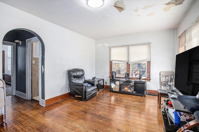 living area featuring baseboards, arched walkways, plenty of natural light, and hardwood / wood-style floors