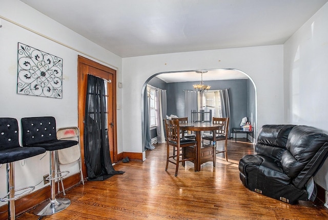 dining area featuring arched walkways, a notable chandelier, baseboards, and wood finished floors