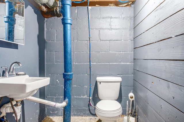 bathroom with toilet, concrete block wall, and a sink