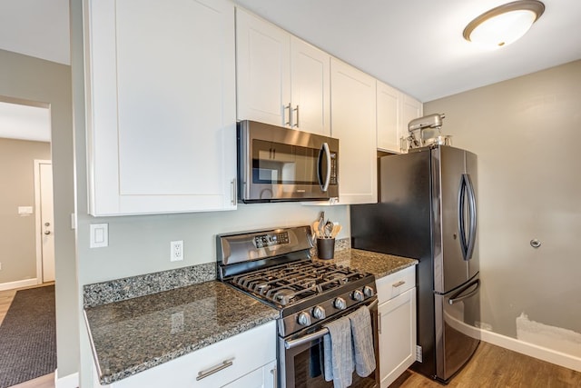 kitchen with dark stone countertops, stainless steel appliances, light wood-style floors, white cabinets, and baseboards