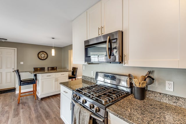 kitchen with dark stone countertops, decorative light fixtures, wood finished floors, white cabinetry, and appliances with stainless steel finishes