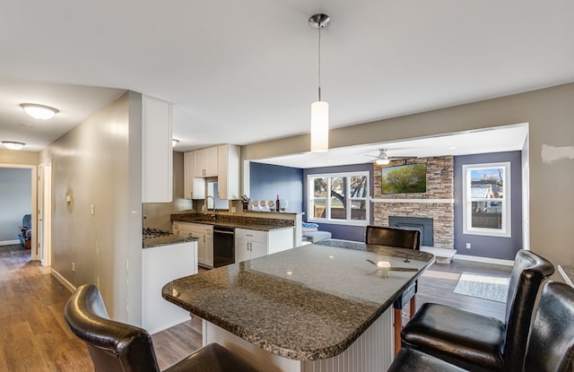 kitchen with dark wood finished floors, a stone fireplace, white cabinets, and a kitchen bar