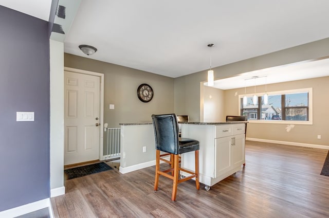 kitchen with wood finished floors, dark stone counters, white cabinets, baseboards, and hanging light fixtures